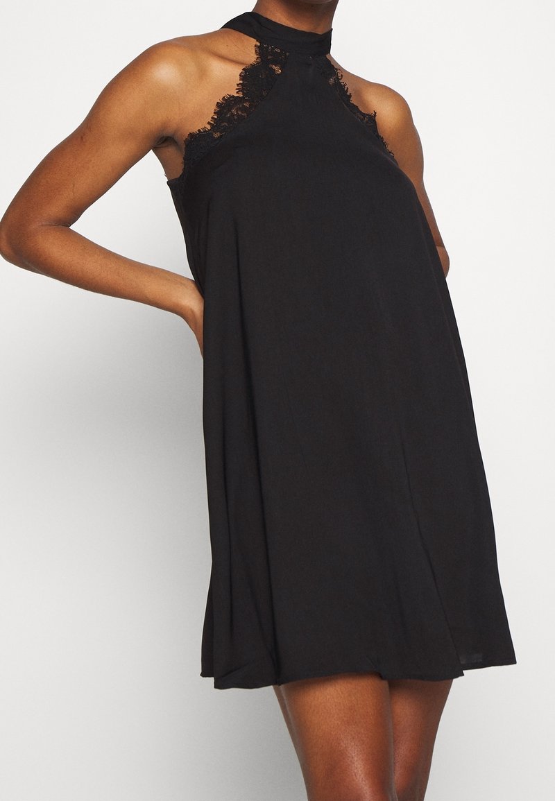 Svart halterneck-klänning i lätt tyg, med spetsdetaljer vid halsringningen och ärmhålen, samt en lös, flödande silhuett.