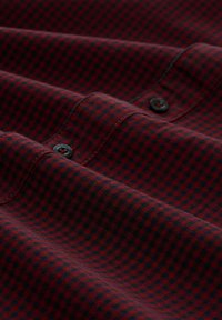 Tissu à carreaux rouge et bleu marine avec un motif texturé, présentant des boutons noirs et des coutures visibles sur une chemise pliée.