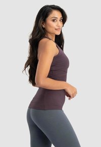 Ärmlös lila linne gjort av ett mjukt, stretchigt tyg, parat med åtsittande grå leggings. Har en slät textur och skräddarsydd passform.