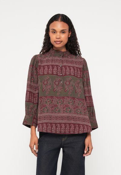 Blouse à manches longues, de couleur bordeaux et verte, avec un col rond, des boutons sur le devant et des manches froncées. Motifs floraux et géométriques.