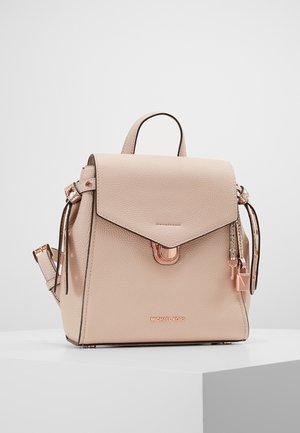 Beżowy skórzany plecak Michael Kors z klapą, różowo-złotymi elementami, regulowanymi paskami oraz ozdobnym brelokiem w kształcie klucza, ustawiony na białej powierzchni.