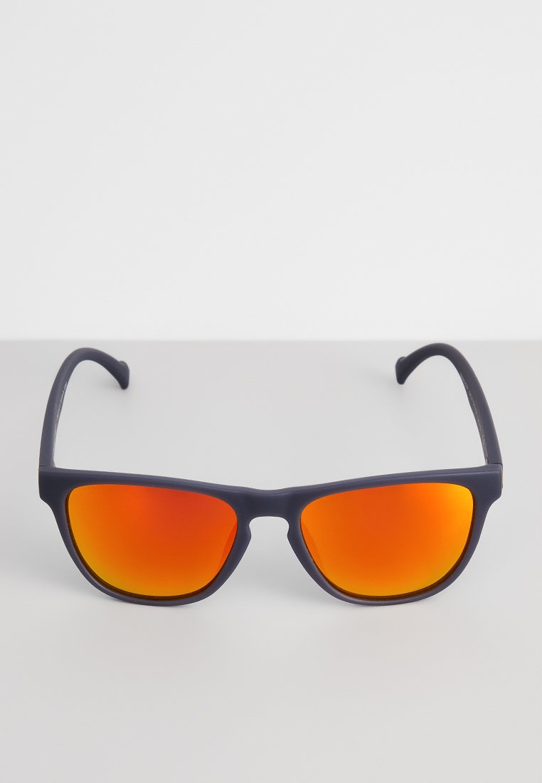 Okulary przeciwsłoneczne z czarnymi oprawkami i jaskrawymi, pomarańczowymi, lustrzanymi soczewkami leżące na gładkiej białej powierzchni.