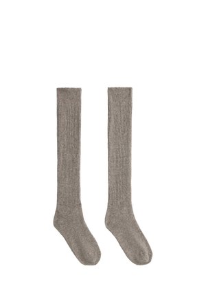 Paire de longues chaussettes grises côtelées, posées à plat, conçues pour couvrir les mollets et les pieds, sur fond blanc.