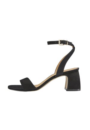 Sandales à talons en suédine noire avec une large sangle avant et une sangle de cheville comportant une boucle en métal doré. Talon carré et texture lisse, mate.