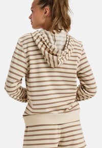 Sudadera beige rayada con capucha forrada y puños acanalados, hecha de una tela suave, con un corte holgado y rayas marrones en contraste.