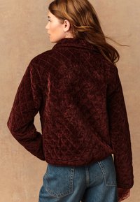 Burgundi värvi tikitud sametise jope kraega, kastikujuline ja tekstuuriga viimistlusega. Disainis on lühendatud pikkus ja laiad varrukad.