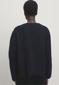 Granatowy, dziany sweter o strukturalnym wykończeniu, z okrągłym dekoltem i luźnymi rękawami, widoczny z tyłu.
