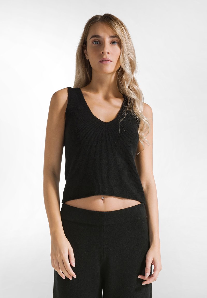 Schwarzes gestricktes Crop-Top mit tiefem V-Ausschnitt, aus strukturiertem Stoff und in lockerer Passform, kombiniert mit hochgeschnittenen schwarzen Hosen.