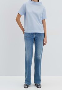 Top azzurro chiaro a maniche corte con motivo testurizzato, abbinato a jeans azzurri chiari a taglio dritto e scarpe grigie lucide.