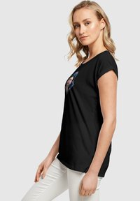 Schwarzes T-Shirt mit kurzen Ärmeln, das ein farbenfrohes grafisches Design mit floralen Akzenten und einem zentralen Porträt zeigt, aus weichem Baumwollstoff gefertigt.