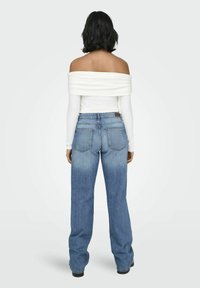 Top blanco sin hombros con mangas largas, combinado con jeans de mezclilla de cintura alta en un lavado claro, con un diseño desgastado y dos bolsillos traseros.