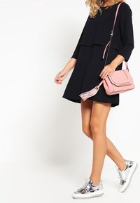 Abito nero a strati con maniche tre quarti, abbinato a una borsa a tracolla rosa chiaro e scarpe da ginnastica con piattaforma in argento metallico.