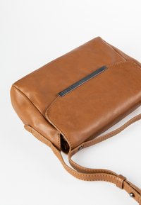 Braune Leder-Crossbody-Tasche mit rechteckiger Form, die ein silbernes Metallakzent auf der Vorderseite und einen langen, verstellbaren Tragegurt hat.