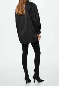 Overmaat zwart shirt met een matte afwerking, lange mouwen en een gebogen zoom, gecombineerd met zwarte high-heeled soklaarzen en goed passende legging.