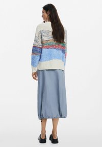 Több színben, kék, krémszínű és piros árnyalatokkal készült kötött pulóver; hosszú, világoskék szoknyával és fekete cipővel párosítva. Texturált és laza szabású.