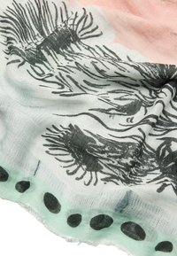 Lekka chusta z abstrakcyjnymi czarnymi wzorami na jasnopłowym i różowym tle, z frędzlami na brzegu i miękkim, teksturowanym wykończeniem.