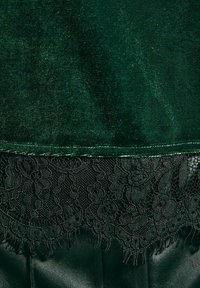 Tissu en velours vert foncé avec un délicat bord en dentelle noire en bas, présentant des motifs floraux et une finition texturée.