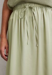 Light green skirt made of soft fabric with an elastic waistband and adjustable tie. The fabric has a smooth texture and flowing design.