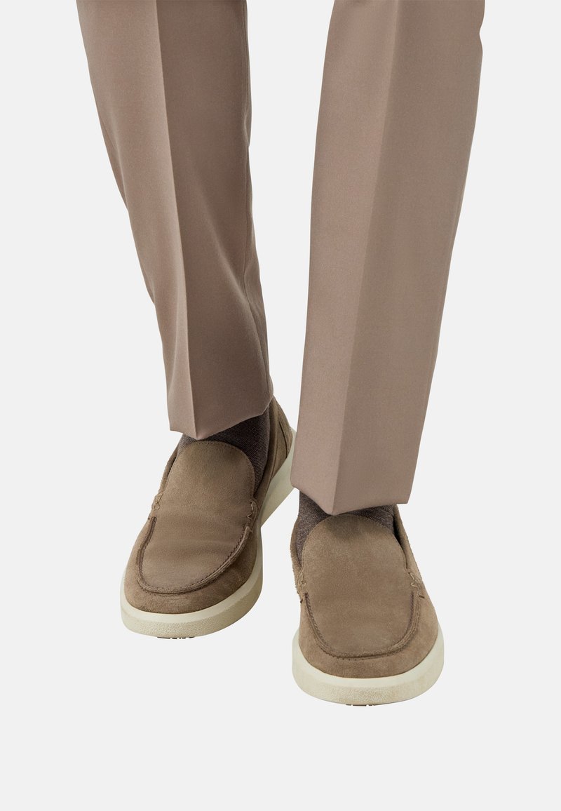 Mees, kes kannab beige nahast slip-on kingi valgete tallade ja pruunide sokkidega, koos sobivate beige pükstega.