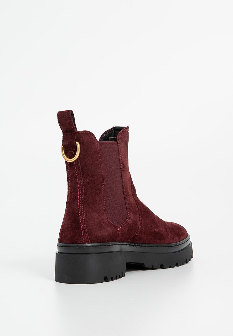 Bordeaux suède enkellaarsjes met elastische zijpanelen, een gouden trekband en een zwarte chunky zool met een geribbelde textuur.