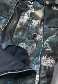 Fleece-gevoerde jas met een reptielen- en dinosaurustextuur op een donkere stof, met een zilveren ritssluiting en Molo-logo.