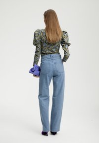 Blusa a fiori con maniche a sbuffo, abbinata a jeans in denim azzurro chiaro a vita alta e una borsa a tracolla viola. Scarpe con tacco in un colore accentato.