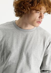 Sudadera gris con escote redondo, hecha de una tela suave. Presenta un cuello acanalado y una textura lisa, mostrando detalles de costura sutiles.
