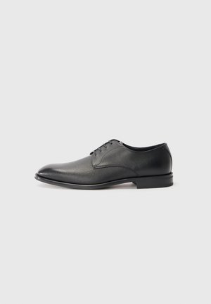 Zapato de vestir para hombre de cuero negro con cordones, tacón bajo y acabado liso, ligeramente texturizado sobre fondo blanco plano.