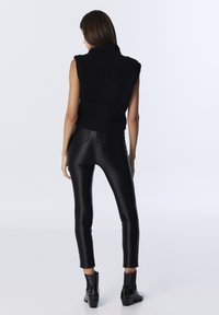 Black sleeveless fleece top with a high collar, paired with fitted black faux leather trousers and ankle boots. Smooth texture and slim fit.