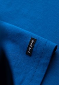 Blauwe katoenen t-shirt met een gladde textuur, voorzien van een zwart stoffen label met witte letters "ombre" op de mouw. Eenvoudig ontwerp.