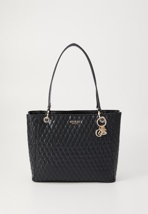 Black quilted handbag made of patent leather with two handles, gold-tone hardware, branded logo, and decorative charms.