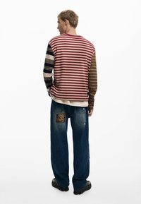Striped long-sleeve shirt with red, brown, and navy colors; relaxed-fit blue jeans with a textured patch. Subtle detail in sleeves.