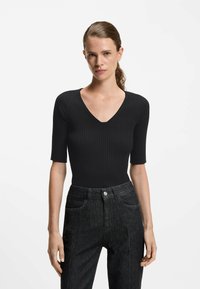 Schwarzes, geripptes Oberteil mit V-Ausschnitt und kurzen Ärmeln, kombiniert mit hoch sitzenden, dunklen Jeans. Strukturiertes Material und figurnahes Design.