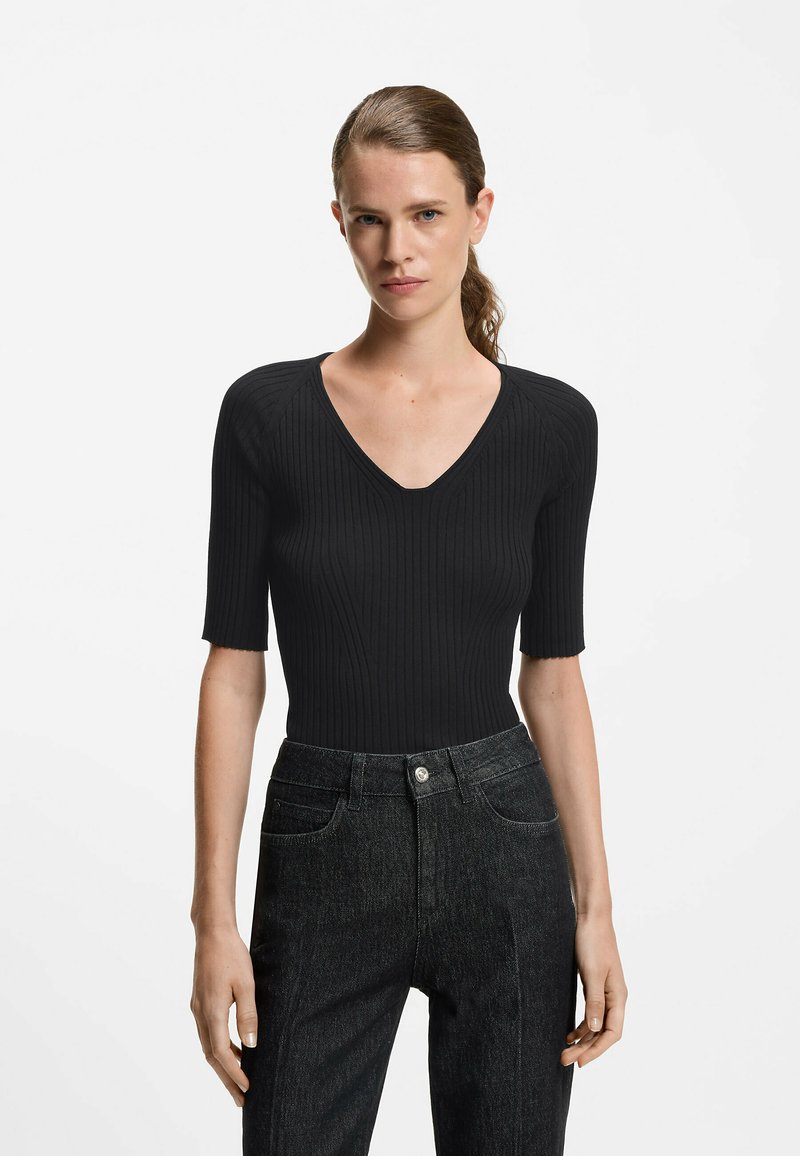 Schwarzes, geripptes Oberteil mit V-Ausschnitt und kurzen Ärmeln, kombiniert mit hoch sitzenden, dunklen Jeans. Strukturiertes Material und figurnahes Design.