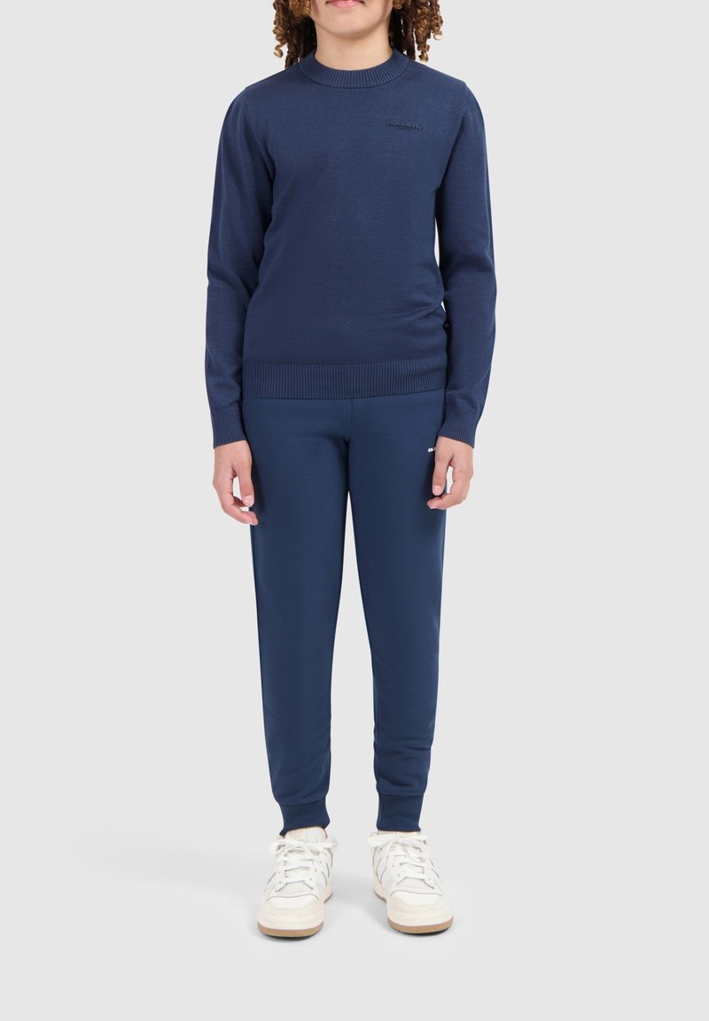 Marineblauer Strickpullover mit rundem Ausschnitt und Rippbündchen, kombiniert mit passenden, schmal geschnittenen Jogginghosen und weißen Sneakern.