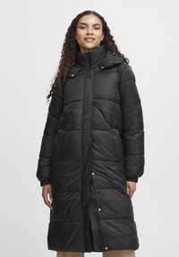 Sort pufferjakke med lang design, der har høj krave, polstrede sektioner, trykknapper og sidelommer. Glat, skinnende tekstur.