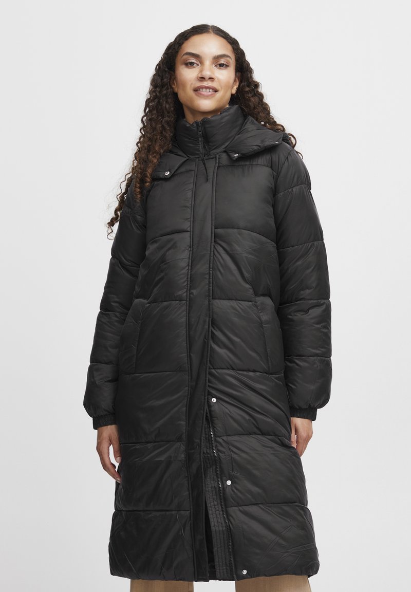 Sort pufferjakke med lang design, der har høj krave, polstrede sektioner, trykknapper og sidelommer. Glat, skinnende tekstur.