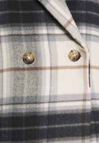 Ullrutig dubbelknäppt kappa i nyanser av grått, beige och brunt med två stora runda knappar och en mjuk textur.