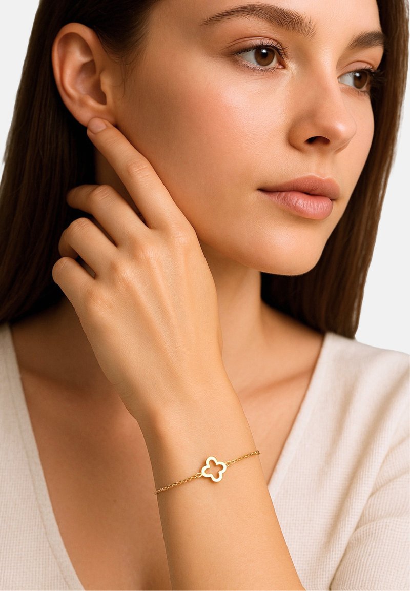 Zlati zapestnica s geometrijskim cvetličnim obeskom. Zapestnica ima zvit dizajn in subtilen sijaj, leži na svetli polti.