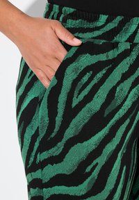 Gröna och svarta mönstrade byxor med ett zebramönster, tillverkade av ett texturerat material, med elastisk midja och sidofickor.