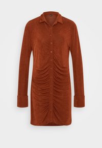 Vestido de camisa de mangas longas na cor ferrugem, com um design de botão na frente e lados franzidos para textura. Feito de um tecido macio e ligeiramente texturado.
