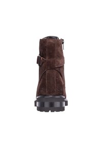 Rjavi semiš gležnjar z teksturirano površino, bočnim zadrgo in robustnim črnim gumijastim podplatom. Opremljen z nastavljivo zaponko za dodatno okrasitev.