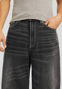 Jeans de mezclilla negra con un corte relajado, que cuentan con costuras de contraste, cinco bolsillos y un ligero desvanecimiento en la parte frontal para dar textura.