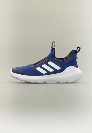 Zapatilla deportiva azul y azul marino sin cordones con suela blanca y tres franjas blancas en el lateral, con costuras naranjas y tiradores en el talón y la lengüeta.