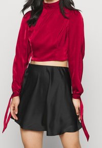 Červený saténový top s krátkými rukávy a mašlemi, v kombinaci s černou saténovou sukní do zvonku. Hladká textura; přiléhavý střih.