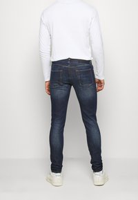 Mörkblå jeans med smal passform, utrustade med två bakfickor och kontrasterande sömmar, tillsammans med en vit långärmad skjorta och vita sneakers.