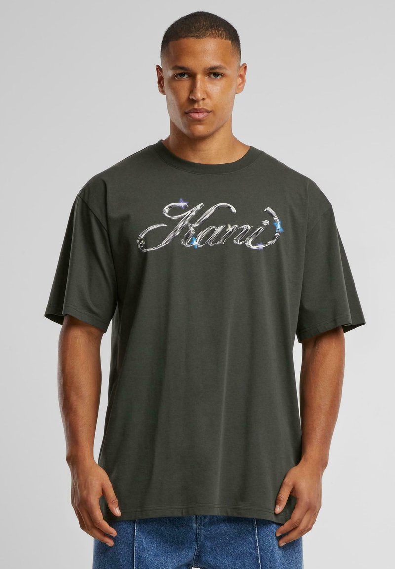 Dark green oversized t-shirt with a round neckline and short sleeves; features a metallic, reflective logo on the front.