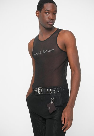 Μαύρο διαφανές τοπ με κεντημένο λογότυπο. Συνδυασμένο με παντελόνι με ψηλή μέση, που διαθέτει μια ζώνη με αμβλύ καρφιά και μια μικρή ετικέτα.