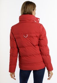 Rode pufferjack met een hoge kraag, gequilte ontwerp en een klein metalen ringdetail aan de achterkant. Soepele textuur en aansluitende mouwen.
