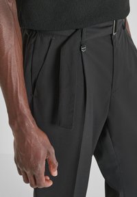 Pantalones negros ajustados con un diseño plisado, que cuentan con tirantes ajustables y una textura elegante y suave. La cintura incluye un broche de metal.